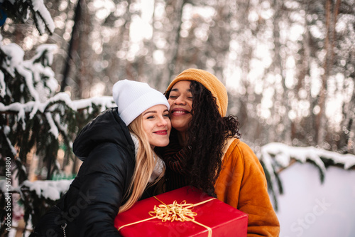 Happy girlfriends holding Christmas present standing by Christmas tree photo