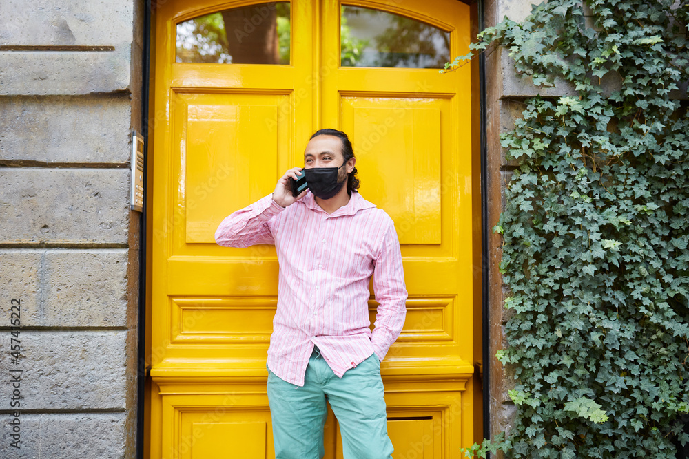young man wearing a face mask while talking on the phone in the street young man wearing a face mask while talking on the phone in the street