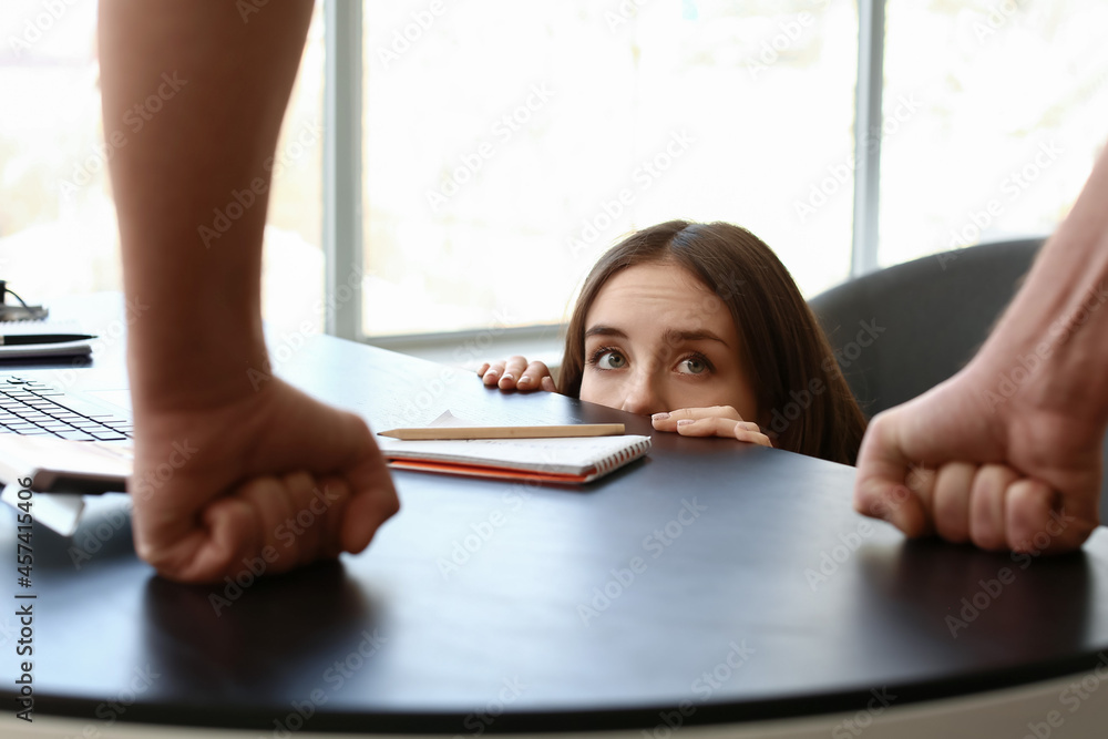 Scared secretary hiding from her boss under table. Concept of