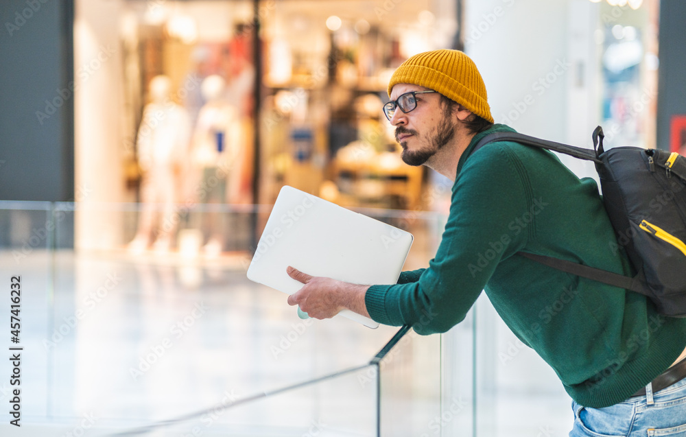 Modern spanish man with glasses and laptop posing in shopping mall Modern spanish man with glasses and laptop posing in shopping mall