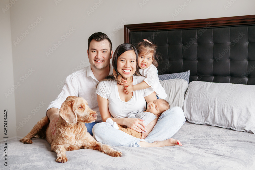 Happy multiracial young family with children kids and dog pet on bed.