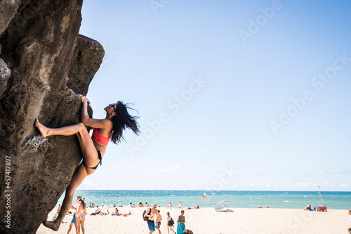 Brunette woman in bikini climbing a rock at the beach on a sunny day photo