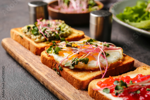 Wooden board with delicious toasts on dark background, closeup