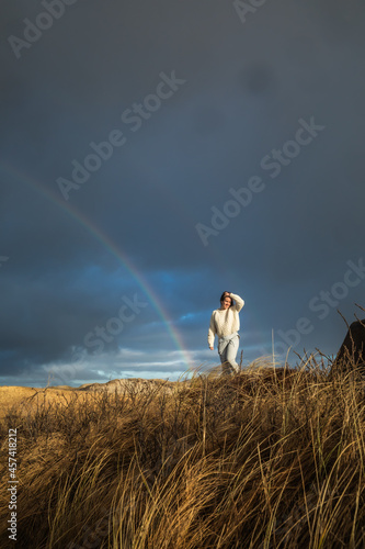 Woman Wearing White Sweater in Tall Grass With Rainbow in Denmark photo