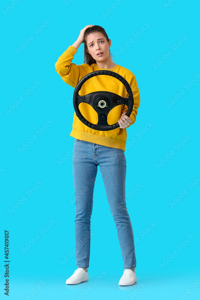 Upset young woman with steering wheel on color background Upset young woman with steering wheel on color background