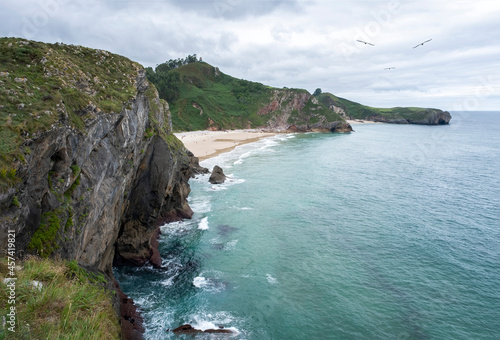 cliffs of Andrin beach in Llanes Asturias Spain, seaside scenery with turquoise waters, green cliffs and a whitish sandy beach photo