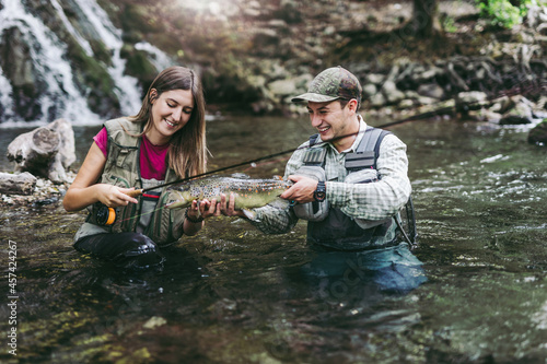 A young couple fishes on a fast mountain river and holds a trout in their hand. The concept of sports fishing.