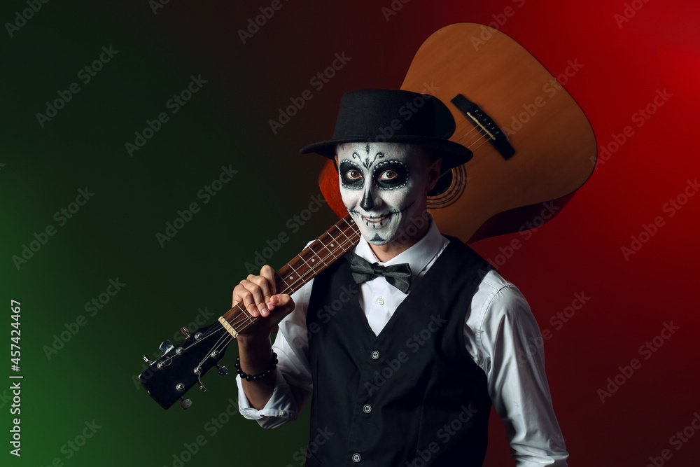 Obraz premium Young man with painted skull on his face and guitar against dark background. Celebration of Mexico's Day of the Dead (El Dia de Muertos)