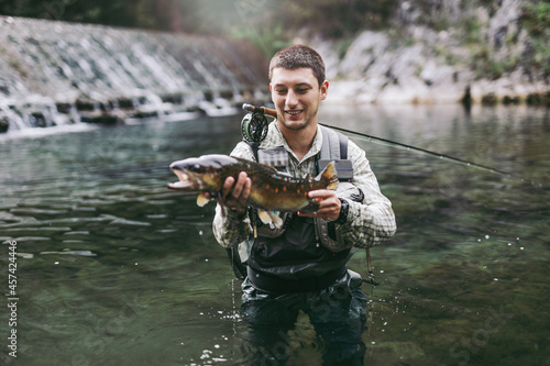 Man, who does sports fishing, fishes on a fast mountain river and holds a trout she caught in his hand.