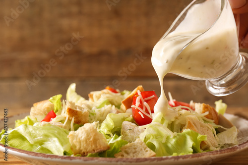 Foto Adding sauce onto plate with tasty Caesar salad on wooden background, closeup