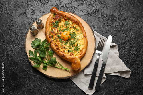 Wooden board with tasty Ajarian khachapuri on dark background