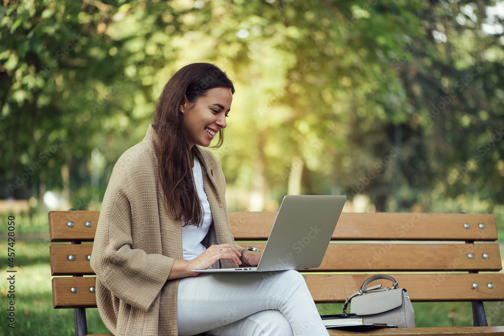 Young pretty woman sitting on bench at the park during summer day and using laptop. Young pretty woman sitting on bench at the park during summer day and using laptop.