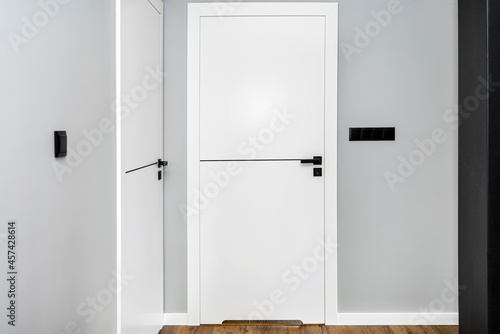 A white door with a ventilation undercut with a matte black handle and a black line in the middle in a modern house with vinyl panels on the floor.