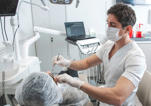 Odontólogo con barbijo en su consultorio atiende la consulta de un paciente photo
