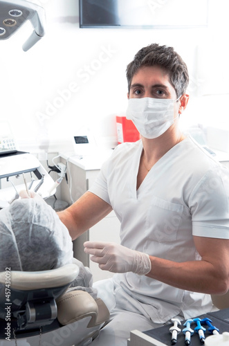 Retrato de un odont  logo con barbijo en su consultorio atiende la consulta de un paciente