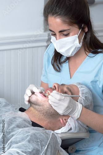 Mujer Odontóloga, revisa la boca abierta de un hombre en el consultorio con un espejo odontológico	 photo