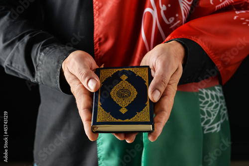 Man with flag of Afghanistan and Koran on dark background, closeup photo