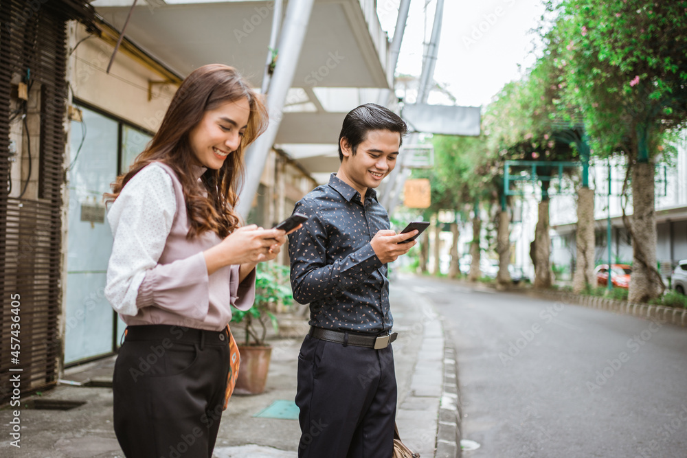 man and woman standing on a sidewalk smiling using their phone man and woman standing on a sidewalk smiling using their phone