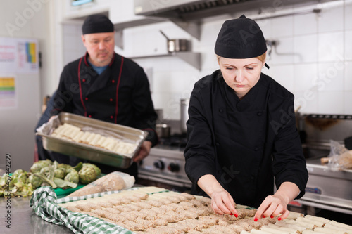 Skilled female cook preparing traditional cannelloni stuffed with mincemeat in restaurant kitchen