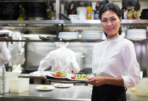 portrait of happy female waitress standing in white kitchen in cafe