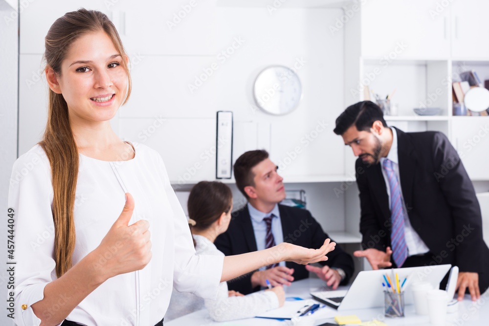 Fototapeta premium Confident smiling businesswoman with team in office showing thumbs up