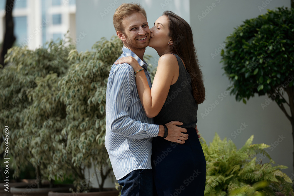 Pretty young woman with long hair kissing her happy boyfriend on cheek