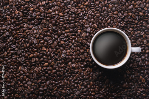 The coffee is in a white cup surrounded by many coffee beans, with copy space.