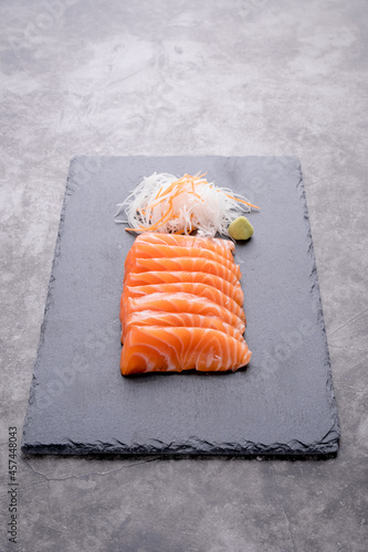 The salmon sashimi was laid out on a black stone plate on an old table, with copy space.