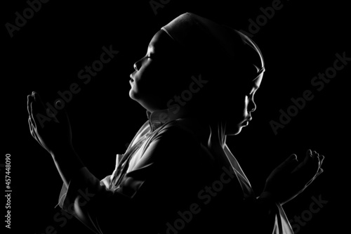 The image of an Asian Muslim boy and girl who is praying with tranquility and faith, with the light from the studio lights from behind, with copy space. © maya1313