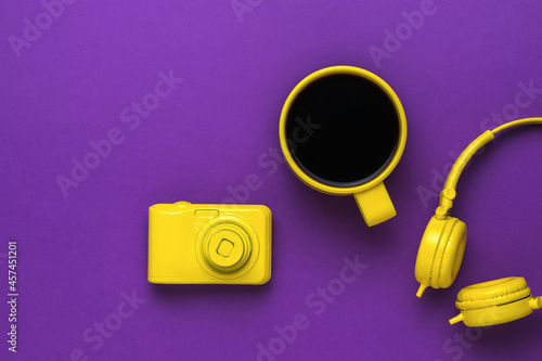 Camera, coffee mug and headphones on a purple background. Color trend.