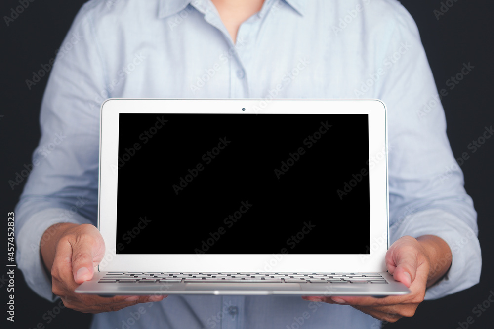 Businessman holding a laptop with a blank screen while standing with black background in the studio Businessman holding a laptop with a blank screen while standing with black background in the studio