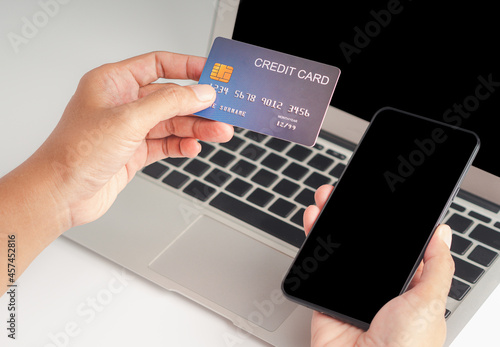 Close-up of hand holding a credit card and smartphone for shopping online with a laptop. Business, e-commerce, and payment concept