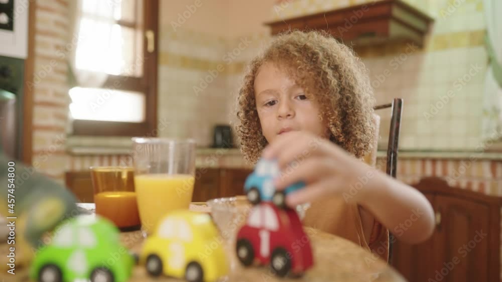 Adorable Kid Playing Car Toys On The Table With Glass Of Juice Drink For Breakfast. medium shot
