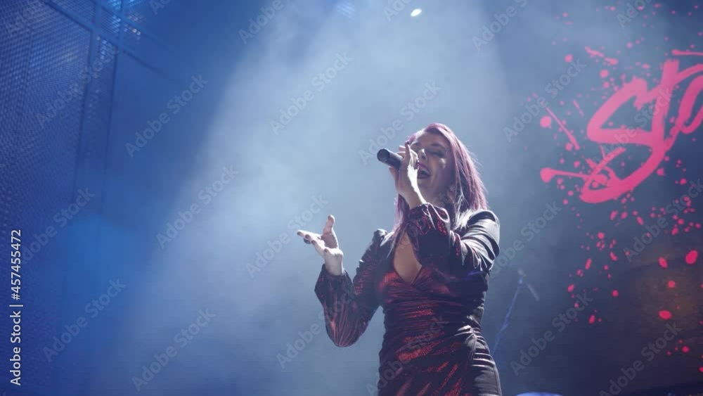 A smoke-filled nightclub or cabaret and a female performer singing into a cordless microphone and using hand gestures. A smoke-filled nightclub or cabaret and a female performer singing into a cordless microphone and using hand gestures.