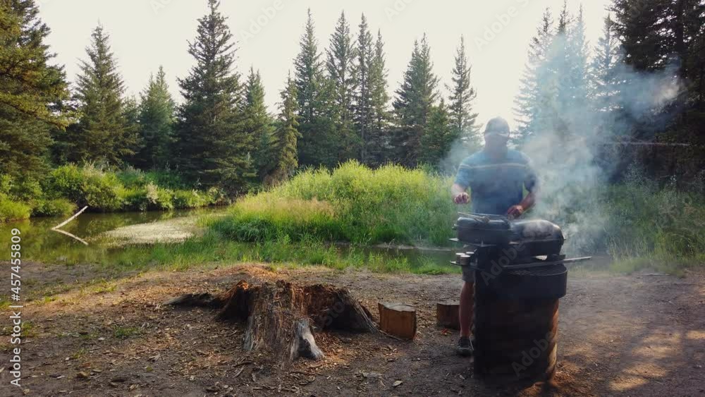 Barbecue with a view - caucasian man grilling meat in the outdoors, next to river Barbecue with a view - caucasian man grilling meat in the outdoors, next to river