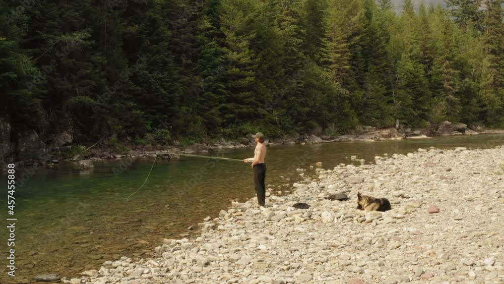 Fly-fishing at McDonald Creek in Glacier National Park - A man fly-casting whilst his loyal dog waits patiently on the bank. Fly-fishing at McDonald Creek in Glacier National Park - A man fly-casting whilst his loyal dog waits patiently on the bank.
