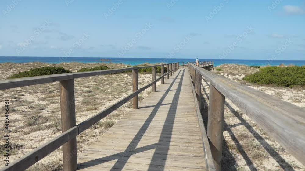 Man tourist walking alone at the end of a long wooden bridge that goes towards the sea, sunny day. Man tourist walking alone at the end of a long wooden bridge that goes towards the sea, sunny day.