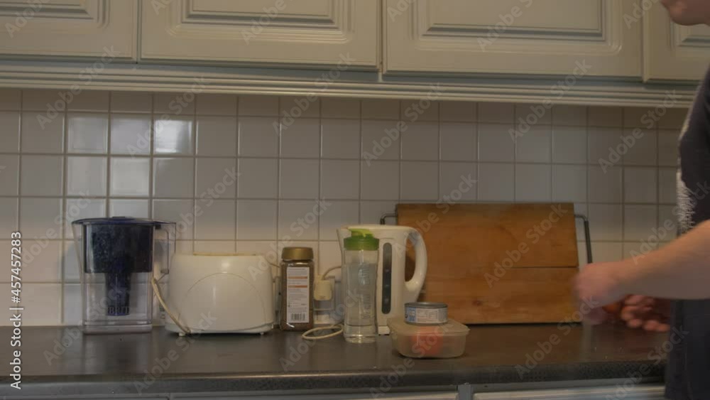 Man places water bottle on kitchen counter with prepared lunchbox Man places water bottle on kitchen counter with prepared lunchbox