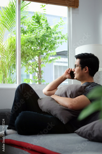 Young man talking on mobile phone and looking out of window while sitting on sofa.