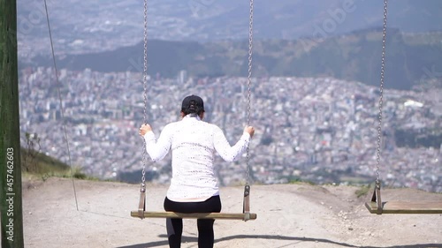 Slow motion of a woman swinging on a swing on top of a mountain with the view of the city Quito, Ecuador.
