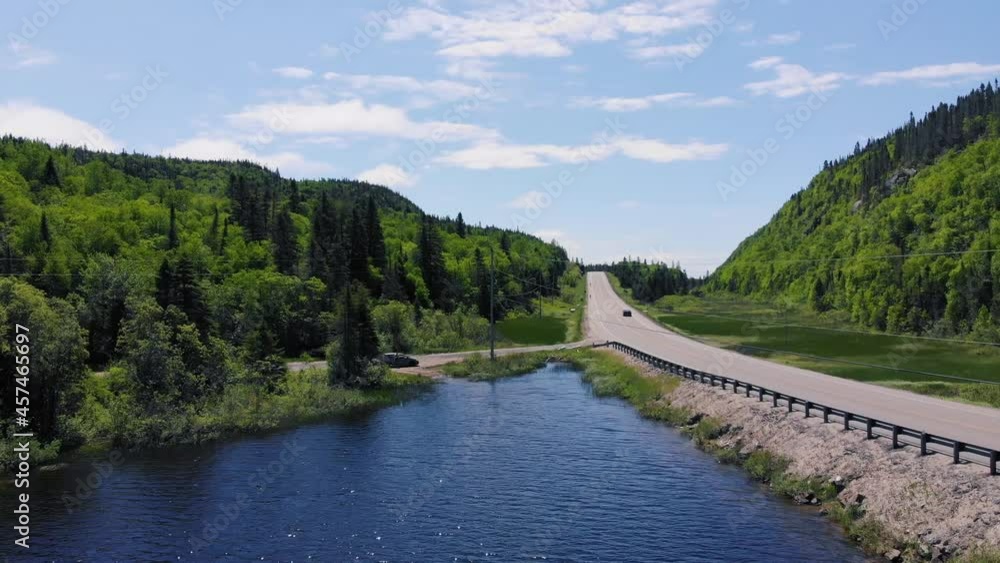 A white semi truck drives down a highway surrounded by forests and mountains next to a lake during the day in Ontario, Canada. A white semi truck drives down a highway surrounded by forests and mountains next to a lake during the day in Ontario, Canada.
