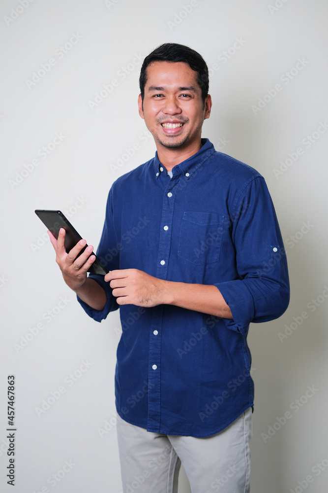 Young Asian man holding mobile tablet gadget while smiling confident Young Asian man holding mobile tablet gadget while smiling confident