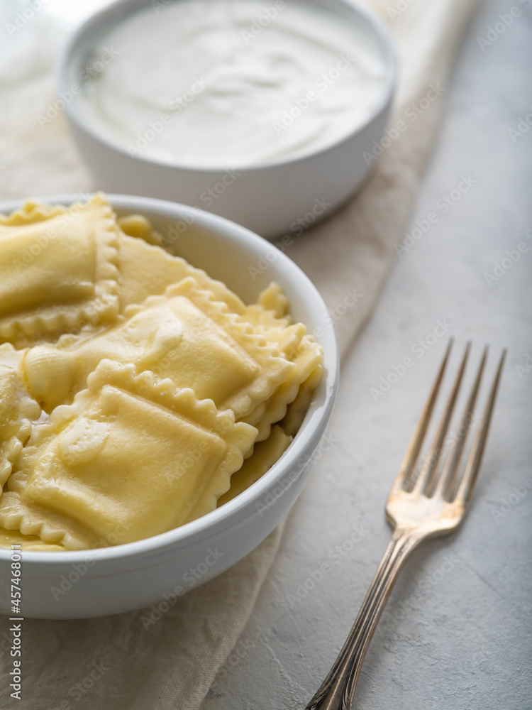 Serving ravioli on a white plate and fork. In the background is a bowl of sour cream. White napkin. Light background. Close-up. Restaurant, hotel, cafe, home cooking.