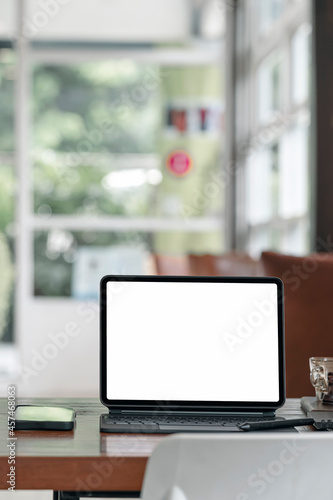 Blank white screen tablet with magic keyboard on wooden table in modern living room. © NAMPIX