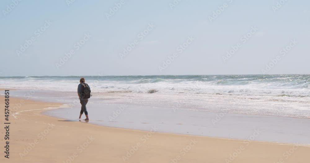 Young woman with a backpack walks along a sandy beach from behind Young woman with a backpack walks along a sandy beach from behind
