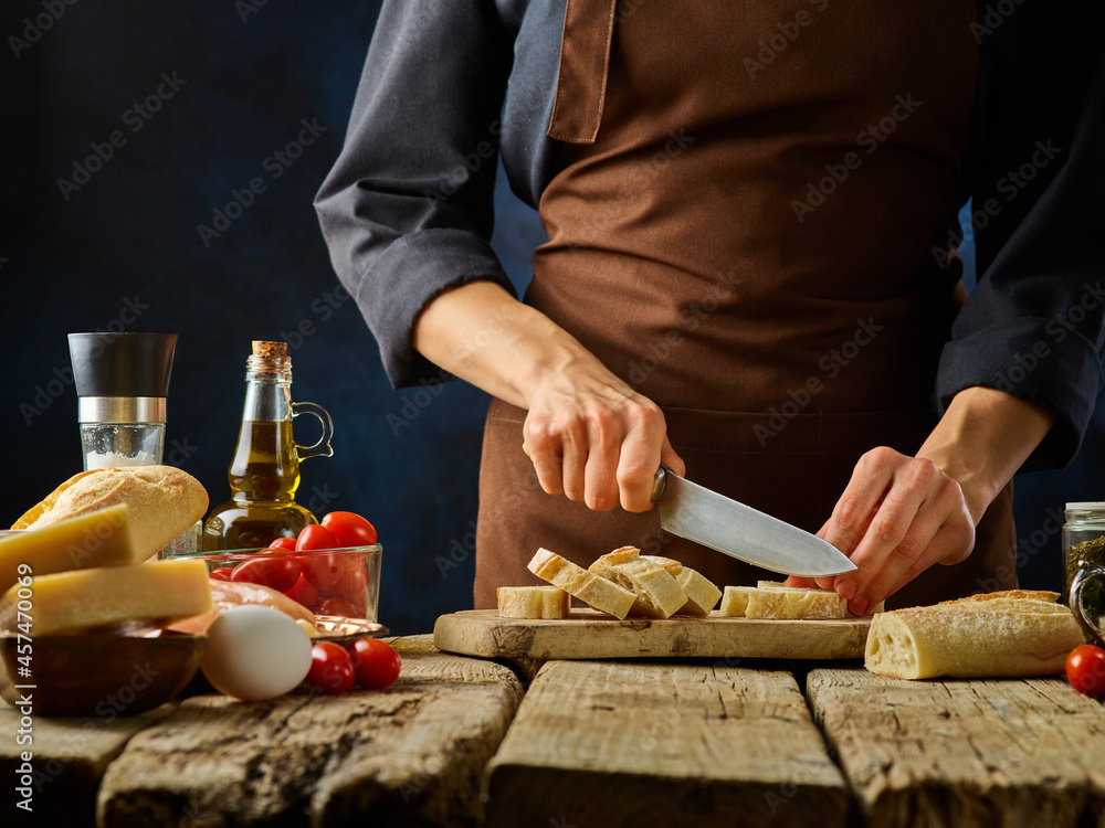 The chef cuts the bread into slices on a cutting board. He prepares the classic Caesar salad. All the ingredients are on a wooden table side by side. Cooking, restaurant, hotel, home cooking. The chef cuts the bread into slices on a cutting board. He prepares the classic Caesar salad. All the ingredients are on a wooden table side by side. Cooking, restaurant, hotel, home cooking.