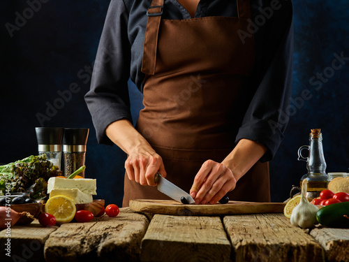 The chef cuts olives for the Greek vitamin salad. Ingredients. Diet food, low-calorie meal, sports nutrition. Restaurant, hotel, culinary blog, recipe book, advertisement, menu design.