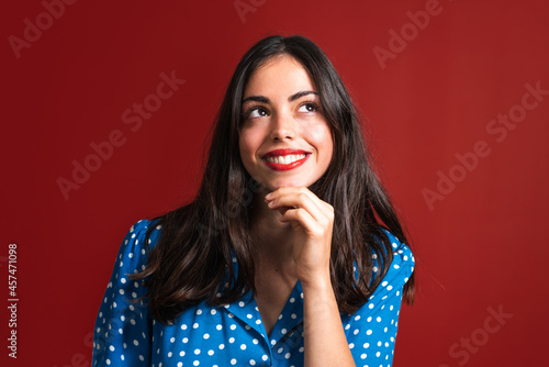 Young female with a wide smile and red lipstick looking up on the red background