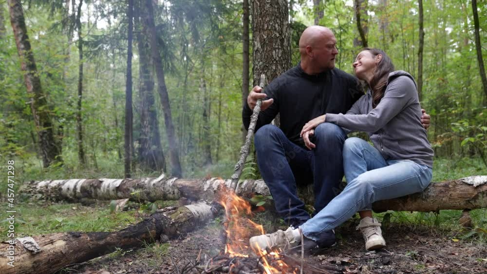 A loving couple of tourists on a camping trip in the forest by the fire hug and kiss