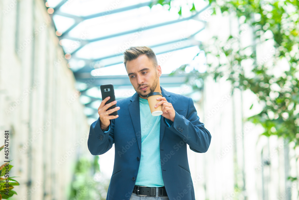 A young successful businessman is working outdoor using smartphone. Man in a casual wear. Business, freelance and remote work.